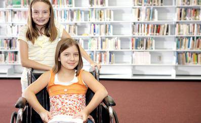 Two school girls at the library. One is in a wheelchair.