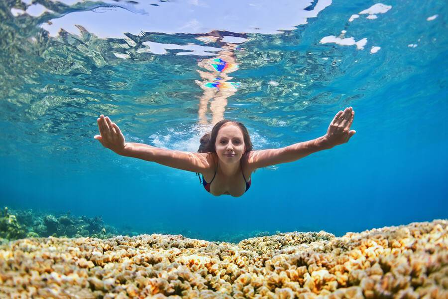 Happy beautiful girl - young woman dive underwater with fun over coral reef in sea pool. Healthy active lifestyle people water sport outdoor activity and swimming lessons on beach summer holidays.