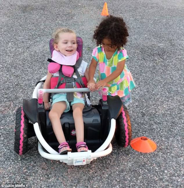 Abby guides Rosie's hand onto the handlebar as she shows her how to use the new wheelchair